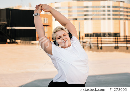 Happy woman with plus size body doing warming up exercises before workout Happy woman with plus size body doing warming up exercises before workout 74278003