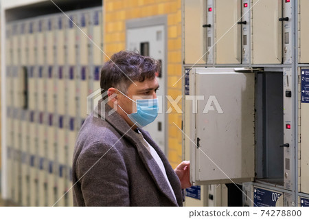 Male traveler wearing a protective surgical mask opening or closing a train station locker cabinet Male traveler wearing a protective surgical mask opening or closing a train station locker cabinet 74278800