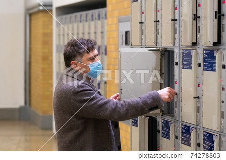 Male traveler wearing a protective surgical mask opening or closing a train station locker cabinet Male traveler wearing a protective surgical mask opening or closing a train station locker cabinet 74278803
