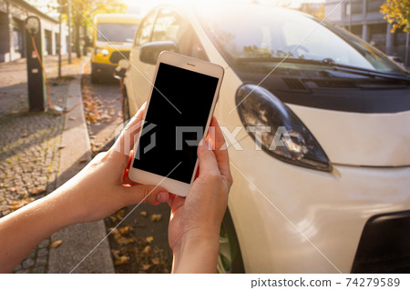 Hands with smartphone on a background of rental car at the charging station Hands with smartphone on a background of rental car at the charging station 74279589