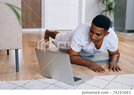 Close-up of strong African-American man exercising workout in horizontal plank position using laptop Close-up of strong African-American man exercising workout in horizontal plank position using laptop 74281663