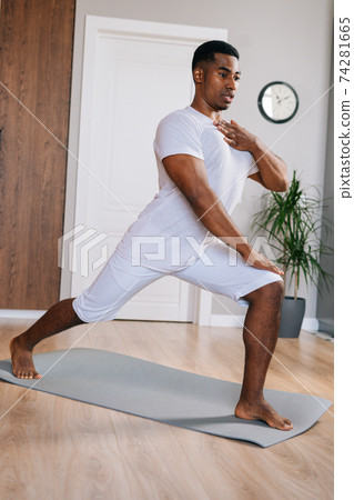 Muscular fit African-American man making sport fitness exercise standing on yoga mat. Muscular fit African-American man making sport fitness exercise standing on yoga mat. 74281665