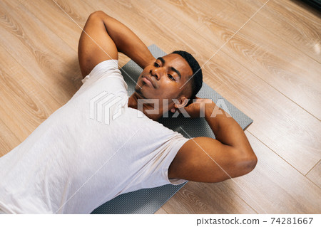 Top view of fit African-American man practicing abs crunches, training abdominal muscles on floor. Top view of fit African-American man practicing abs crunches, training abdominal muscles on floor. 74281667