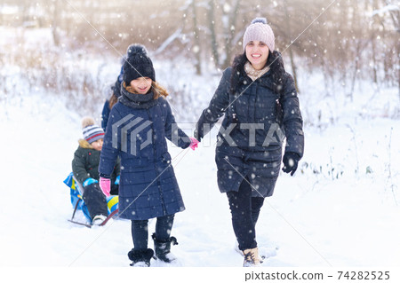 family plays and sleigh rides in winter outdoor, mother and children having fun on snowy winter 74282525