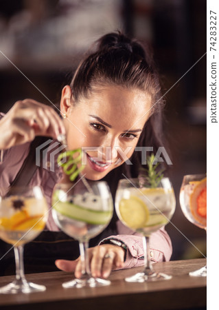 Bartender loving her job decorates gin tonic cocktails in glasses on a bar Bartender loving her job decorates gin tonic cocktails in glasses on a bar 74283227