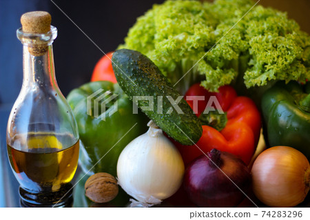 Preparations for a wonderful vegetarian dinner. Washed Bulgarian pepper, green cucumbers, onions, garlic, lettuce leaves and a bottle of olive oil 74283296