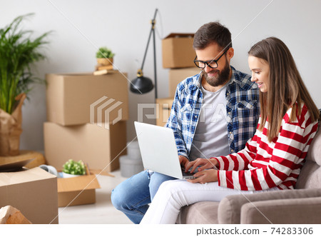 Smiling couple using laptop after relocation in new house 74283306