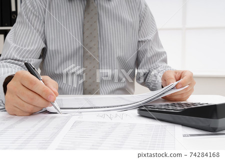 business concept - businessman's working table close view, checks financial reports, writes and counts business concept - businessman's working table close view, checks financial reports, writes and counts 74284168