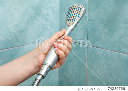 Shower head in human hand on background of tiles in bathroom. Shower head in human hand on background of tiles in bathroom. 74286766
