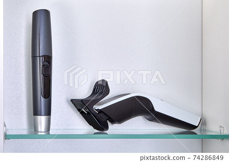 Rechargeable hairclipper is stored on shelf of your bathroom cabinet with cordless trimmer to remove hair from nose and ears. 74286849