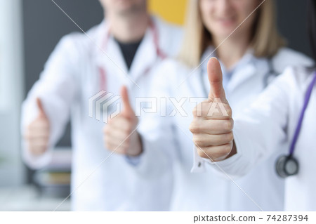 Three doctors stand behind each other and hold their thumbs up 74287394