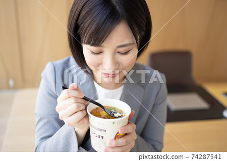 Woman eating cup noodles in the office Woman eating cup noodles in the office 74287541