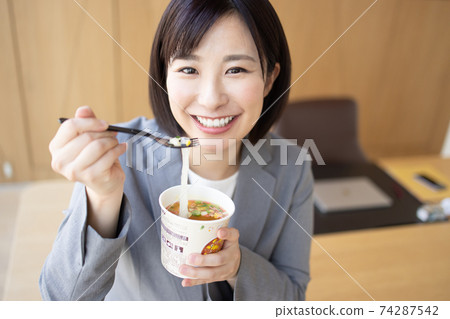 Woman eating cup noodles in the office Woman eating cup noodles in the office 74287542