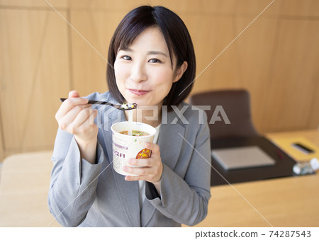 Woman eating cup noodles in the office Woman eating cup noodles in the office 74287543