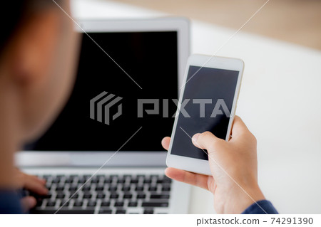 Hand of young man working with laptop computer and smartphone mockup on desk at home. Hand of young man working with laptop computer and smartphone mockup on desk at home. 74291390