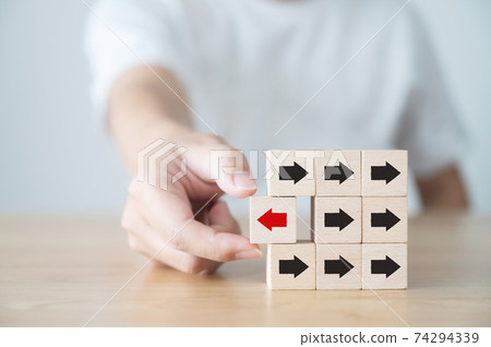 Hand holding wooden block with red arrow facing the opposite direction black arrows 74294339