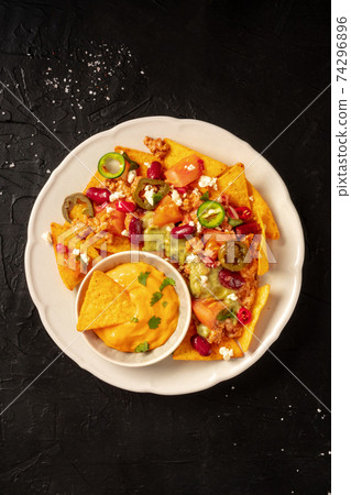 Nachos with beef, guacamole and cheese sauce, top shot on a black background Nachos with beef, guacamole and cheese sauce, top shot on a black background 74296896