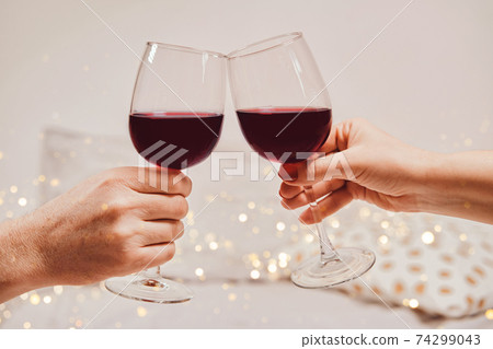 Hands of a man and a woman are holding glasses of wine. Romantic atmosphere, soft focus, bokeh, close-up 74299043