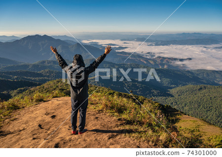 Man hiking raise hand enjoy succeed and looking at mountain range on the top of mountain in tropical forest, Outdoor adventure travel concept Man hiking raise hand enjoy succeed and looking at mountain range on the top of mountain in tropical forest, Outdoor adventure travel concept 74301000