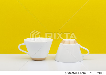 Two white ceramic coffee cups on white table against bright yellow background with space for text Two white ceramic coffee cups on white table against bright yellow background with space for text 74302900