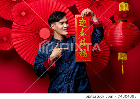 Handsome smiling Asian man in traditional costume holding and pointing 74304395