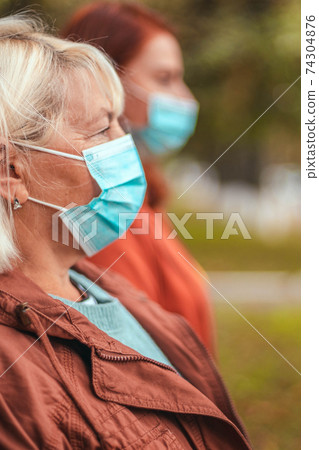 Side view of people in protective medical masks on the street during the coronavirus, gripe or premonia pandemic. Social distancing Side view of people in protective medical masks on the street during the coronavirus, gripe or premonia pandemic. Social distancing 74304876