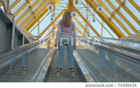 Young woman standing on the escalator Young woman standing on the escalator 74306434
