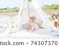 A little cute girl with red curly hair in summer, on the seashore in an airy lace bodysuit and a floral headband in a lace tent, devoried with marine details, shells and cotton. 1st BIRTHDAY.  74307370