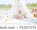 A little cute girl with red curly hair in summer, on the seashore in an airy lace bodysuit and a floral headband in a lace tent, devoried with marine details, shells and cotton. 1st BIRTHDAY.  74307374