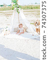 A little cute girl with red curly hair in summer, on the seashore in an airy lace bodysuit and a floral headband in a lace tent, devoried with marine details, shells and cotton. 1st BIRTHDAY.  74307375