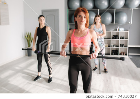 Group of young sporty attractive woman practicing pilates. People standing together. Working out, indoor full length, studio background Group of young sporty attractive woman practicing pilates. People standing together. Working out, indoor full length, studio background 74310027