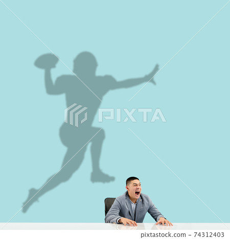 Young man dreaming about future in big sport during his work in office. Becoming a legend. Shadow of dreams on the wall behind him. Copyspace. 74312403