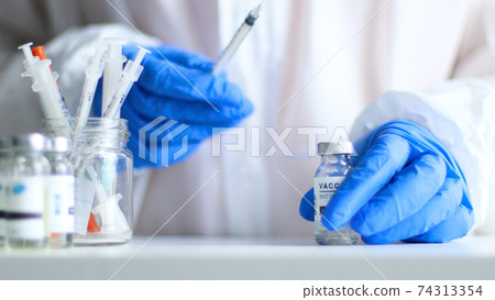 Close up portrait of adult nurse or doctor in medical protective uniform and latex rubber gloves holding syringe with vaccine while preparing for work during coronavirus, flu or measles pandemic for Close up portrait of adult nurse or doctor in medical protective uniform and latex rubber gloves holding syringe with vaccine while preparing for work during coronavirus, flu or measles pandemic for 74313354