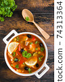 Fish soup with salmon, tilapia, red pepper, onion, carrot, lemon, green and black olives. White casserole on wooden rustic table, top view 74313364