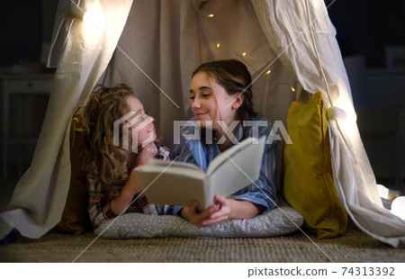 Sisters indoors at home, reading book in pajamas. Lockdown concept. 74313392