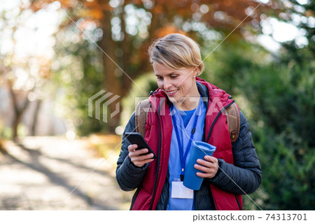 Woman caregiver, nurse or healthcare worker outdoors on the way to work, using smartphone. Woman caregiver, nurse or healthcare worker outdoors on the way to work, using smartphone. 74313701