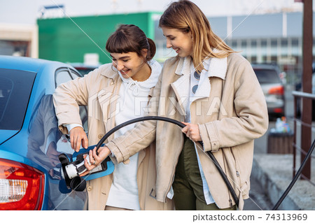 Happy friends refuel car in gas station. Holiday trip 74313969