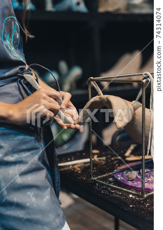 Close-up view of female hands gently handling a clay whale in workshop. Close-up view of female hands gently handling a clay whale in workshop. 74314074