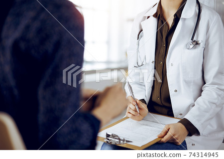 Doctor and patient discussing current health examination while sitting in sunny clinic. Medicine concept 74314945