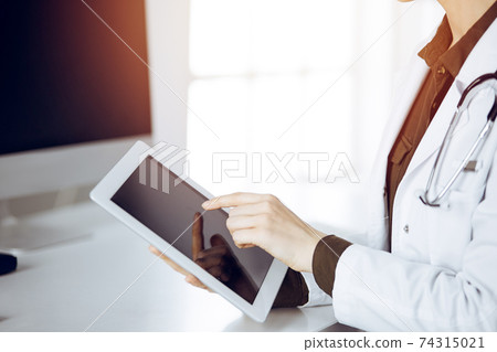 Unknown female doctor using tablet computer in sunny clinic. Medicine concept 74315021