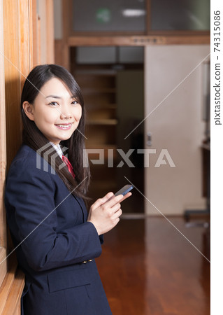 High school girl high school student standing in the corridor with a smartphone High school girl high school student standing in the corridor with a smartphone 74315086
