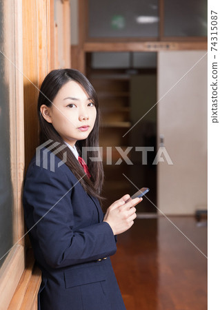 High school girl high school student standing in the corridor with a smartphone High school girl high school student standing in the corridor with a smartphone 74315087