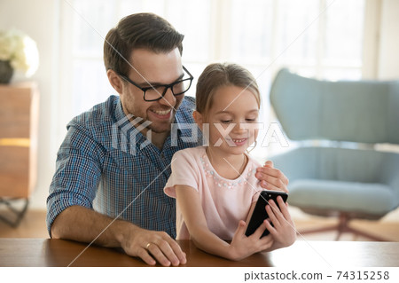 Happy dad and small daughter watch video on cellphone Happy dad and small daughter watch video on cellphone 74315258