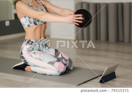 Athletic woman in sportswear does exercises at home. Woman look in tablet while diong exercises. Sport and recreation concept. Healthy lifestyle Athletic woman in sportswear does exercises at home. Woman look in tablet while diong exercises. Sport and recreation concept. Healthy lifestyle 74315371