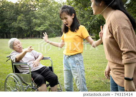 Unhappy asian teen granddaughter dissuade her family from a fight something money,angry senior mother and daughter arguing violently,shouting quarreling at park, borrowing money and not returning it 74315414