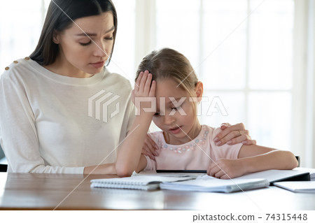 Loving mom support unhappy small girl doing homework 74315448