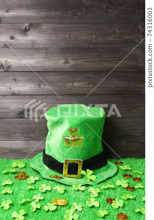 Green leprechaun hat with gold clover leaf, shamrock leaves and leprechaun gold coins on green grass, dark wooden planks background. Saint Patricks Day banner, poster, flyer, invitation template 74316003
