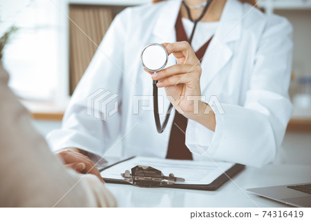 Unknown woman-doctor with a stethoscope in the hands. Physician is ready to examine a patient, close-up of hands. Medicine concept Unknown woman-doctor with a stethoscope in the hands. Physician is ready to examine a patient, close-up of hands. Medicine concept 74316419