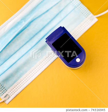 Oximeter and protective medical mask on a gold background. Copy space 74316945