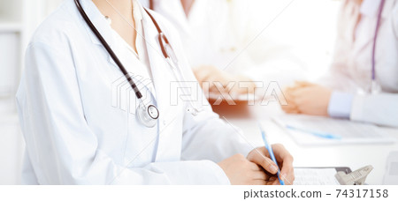 Group of unknown doctors discussing problems to stop coronavirus pandemic while sitting at meeting in clinic, close-up . Medicine concept 74317158